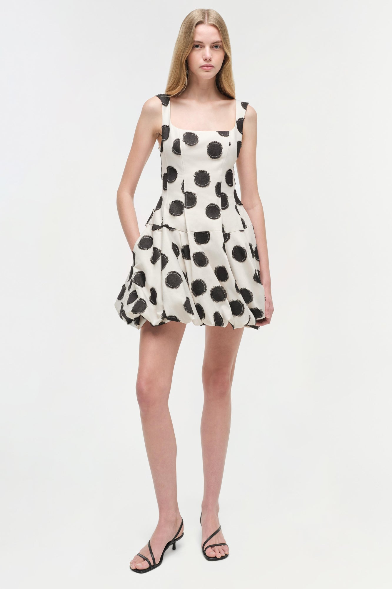 White sleeveless mini dress with black polka dot pattern and gathered skirt.