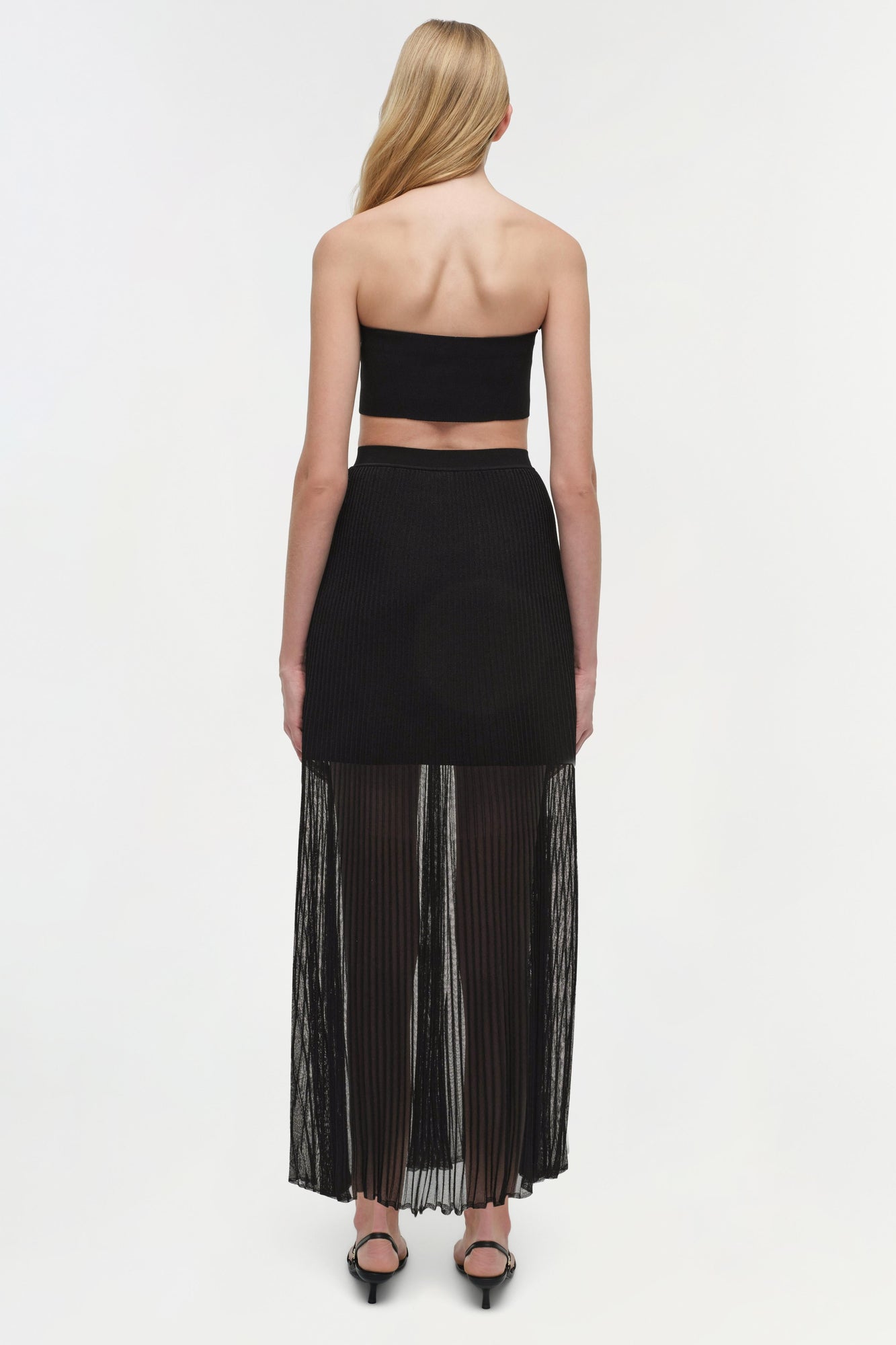 Black knit bandeau bralette with ribbed texture, shown from back on model wearing matching pleated skirt.
