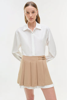 Beige pleated skort with buckle details at waist, paired with white collared button-up shirt.