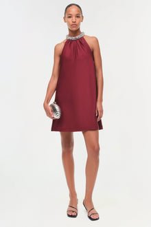 Burgundy halter mini dress with embellished neckline, shown on model wearing black slides and silver clutch.