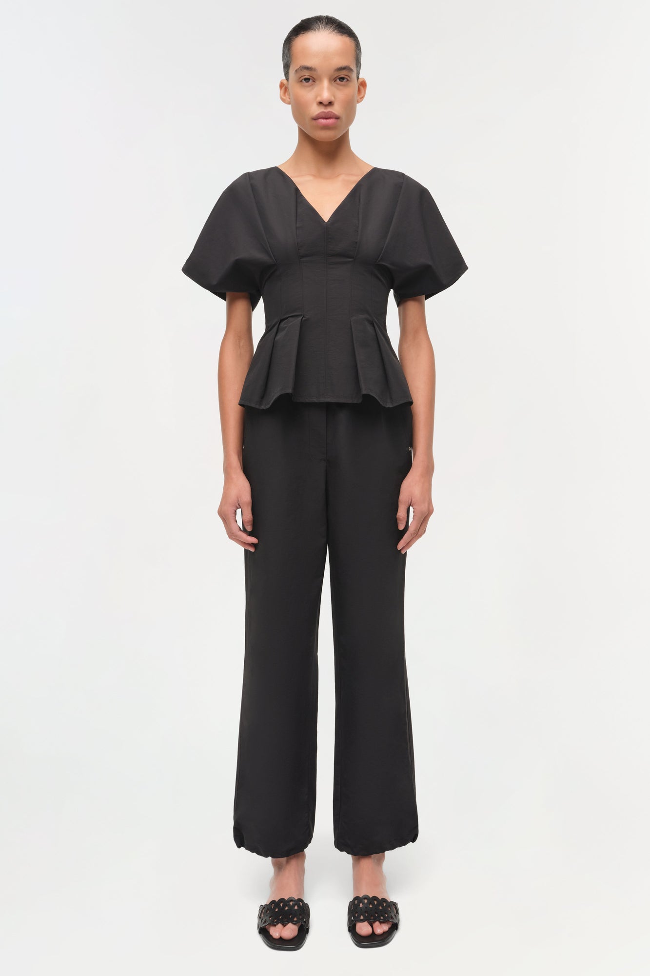 Woman wearing black cotton faille pull-on pants with cropped straight-leg fit and peplum top.
