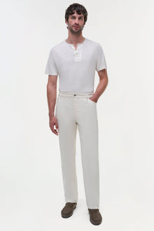 Man wearing cream wide-leg jeans with white henley shirt and brown suede loafers.