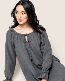A woman with long dark hair models Petite Plumes Womens Flannel Delphine Nightgown in Grey. Featuring long sleeves and a tie at the neckline, she exudes relaxed elegance against a light beige background.