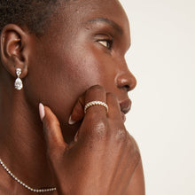 Model. Woman wearing an eternity ring and drop earrings on a neutral background