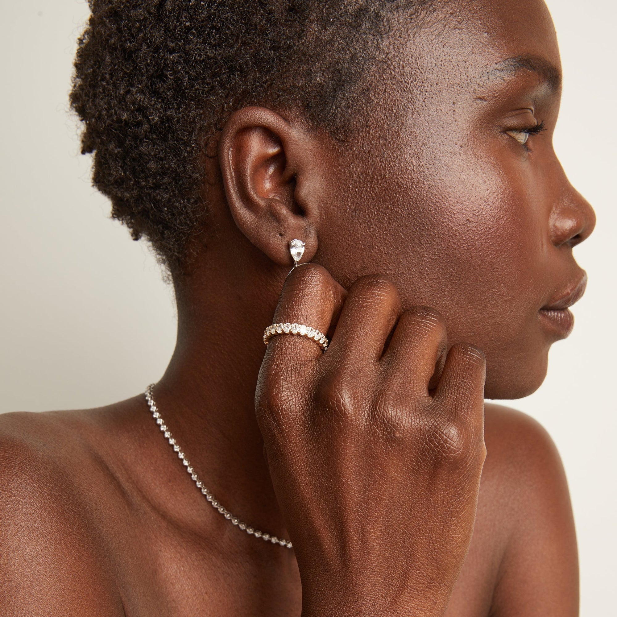 Woman wearing an eternity ring and drop earrings on a neutral background