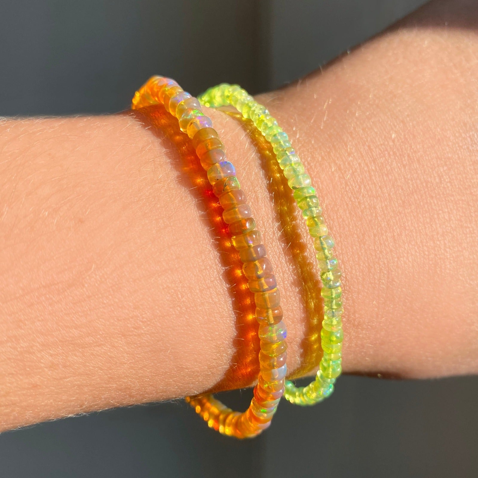 Shimmering Spring Green opal beaded bracelet made of smooth opals in shades of light yellow on a gold linking lobster clasp styled on a wrist with a orange opal bracelet