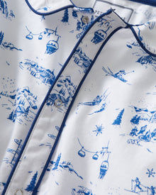 The Baby's Twill Cambridge Romper in Chalet Toile is a white long-sleeve, full-length onesie with blue alpine scene prints and blue piping on the collar, cuffs, and front placket.