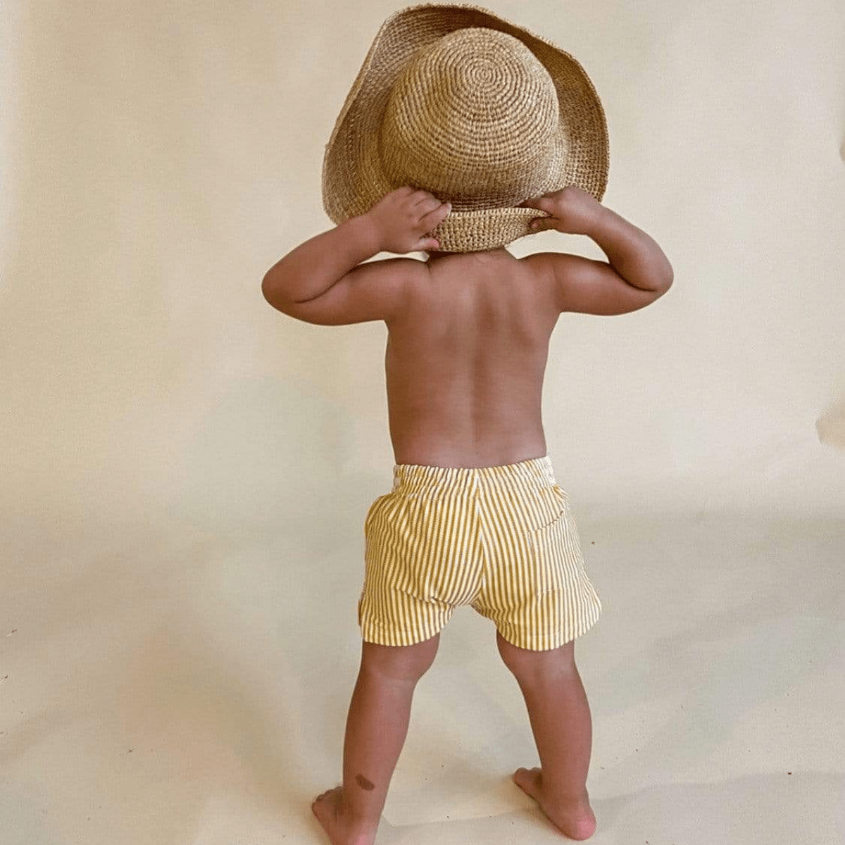 Child wearing yellow and white vertical striped swim trunks, viewed from behind.