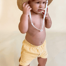 Toddler wearing yellow and white vertical striped swim trunks with white drawstring.