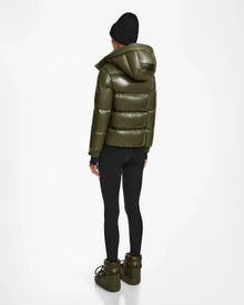 A person in the Rudsak ASHLYN S - 8124565 Loden Green puffer jacket, black leggings, chunky olive boots, and a black beanie stands facing away against a plain white background.