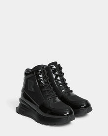 The CHELSA - L224505 Black by Rudsak are women’s sneaker boots with shiny patent leather accents, thick rubber soles, black laces, and side branding—offering a stylish upgrade to classic winter boots. Displayed on a plain white background.
