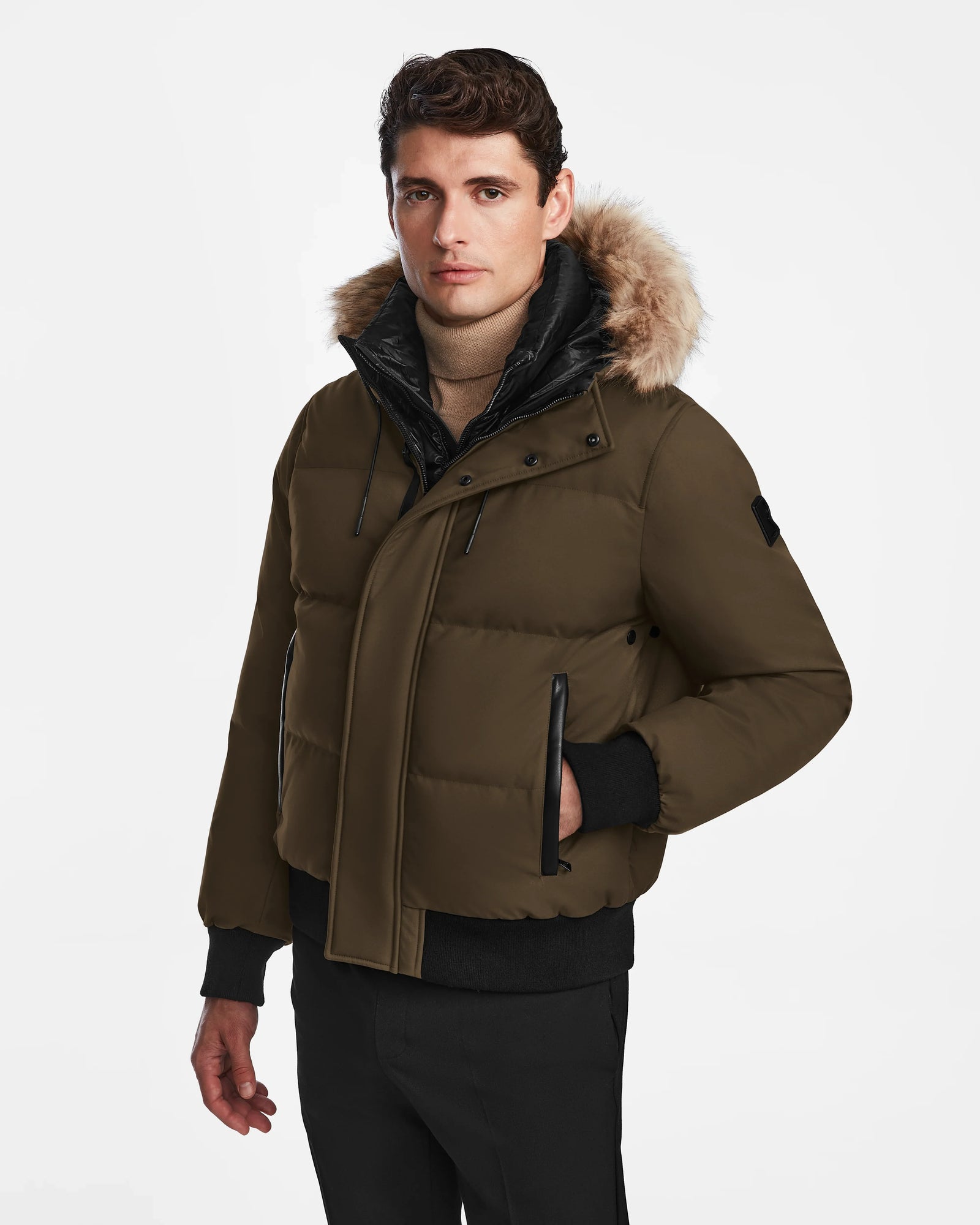 A man in the Rudsak DALLAS - M122501 Army, a weather-resistant brown men's quilted down bomber with fur trim, black inner layer, and black pants stands against a plain white background.
