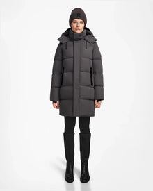 A person faces forward in a long Rudsak JOELLE - 8124729 Grey RDS-certified down puffer coat, with black leggings, boots, and a dark knit beanie. The background is plain white.