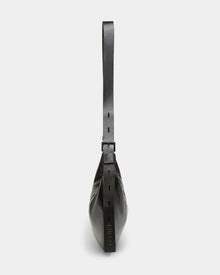 Side view of the Rudsak LANISSA - 8324505 Black leather hobo bag with a wide, adjustable strap and square buckle detail, featuring an embossed logo near the base, shown against a plain white background.
