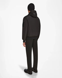Wearing the Rudsak NEVEN - M124520 Black men’s bomber jacket, a person stands facing away in dark dress pants, black beanie, and black shoes against a white background.
