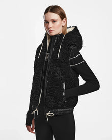 A woman in the RAQUEL S - 8124526 Black ski vest by Rudsak, ready for winter mountain adventures.