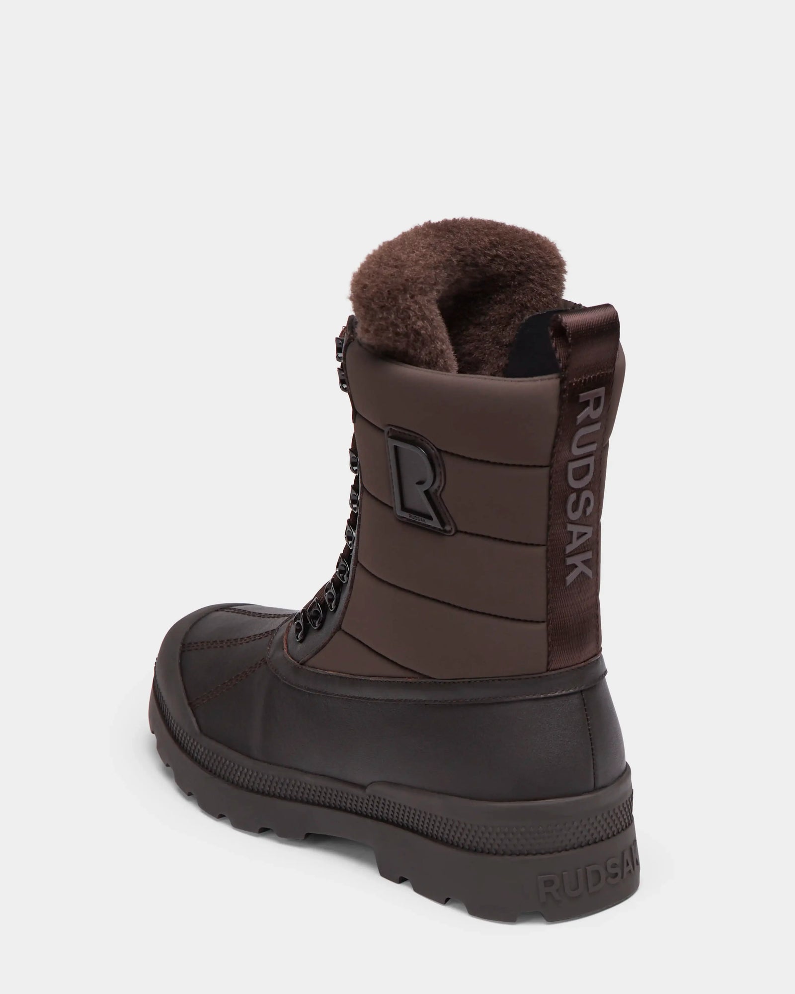 The REAGAN - 6224501 Espresso by Rudsak is a brown mens winter boot with a fur-lined interior, lace-up front, and RUDSAK branding on the heel and pull tab, shown against a plain white background.