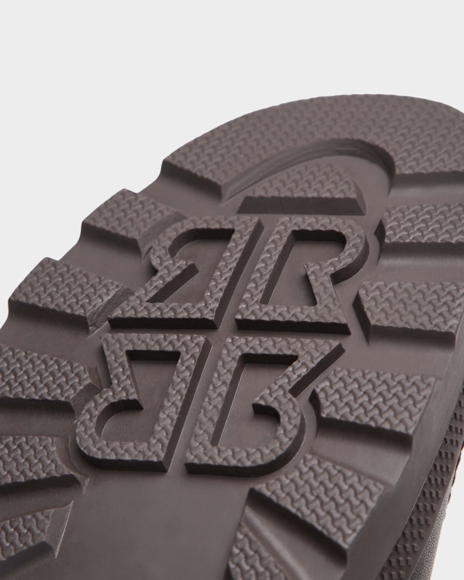 Close-up of a black rubber sole from Rudsak’s REAGAN - 6224501 Espresso men’s winter boots, featuring a bold geometric tread with raised lines, textured sections, and overlapping stylized B shapes at the center.