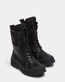 The Rudsak RITA - L222502 Black women's winter boots feature mid-calf lace-up design, weather-treated leather, rugged soles, and embossed branding on the tongue and side, shown on a plain light background.