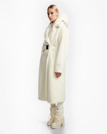 A person poses against a white background wearing the Rudsak TINA - 8123578 Iceland womens faux fur teddy trench coat with a belt, styled with matching boots and light-colored pants.