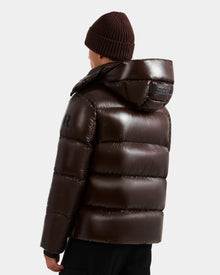 A person wearing the Rudsak DANIEL S - M124508 Espresso men's hooded down puffer, featuring a weather-resistant glossy shell, with a brown knit beanie, is seen from behind against a plain white background.