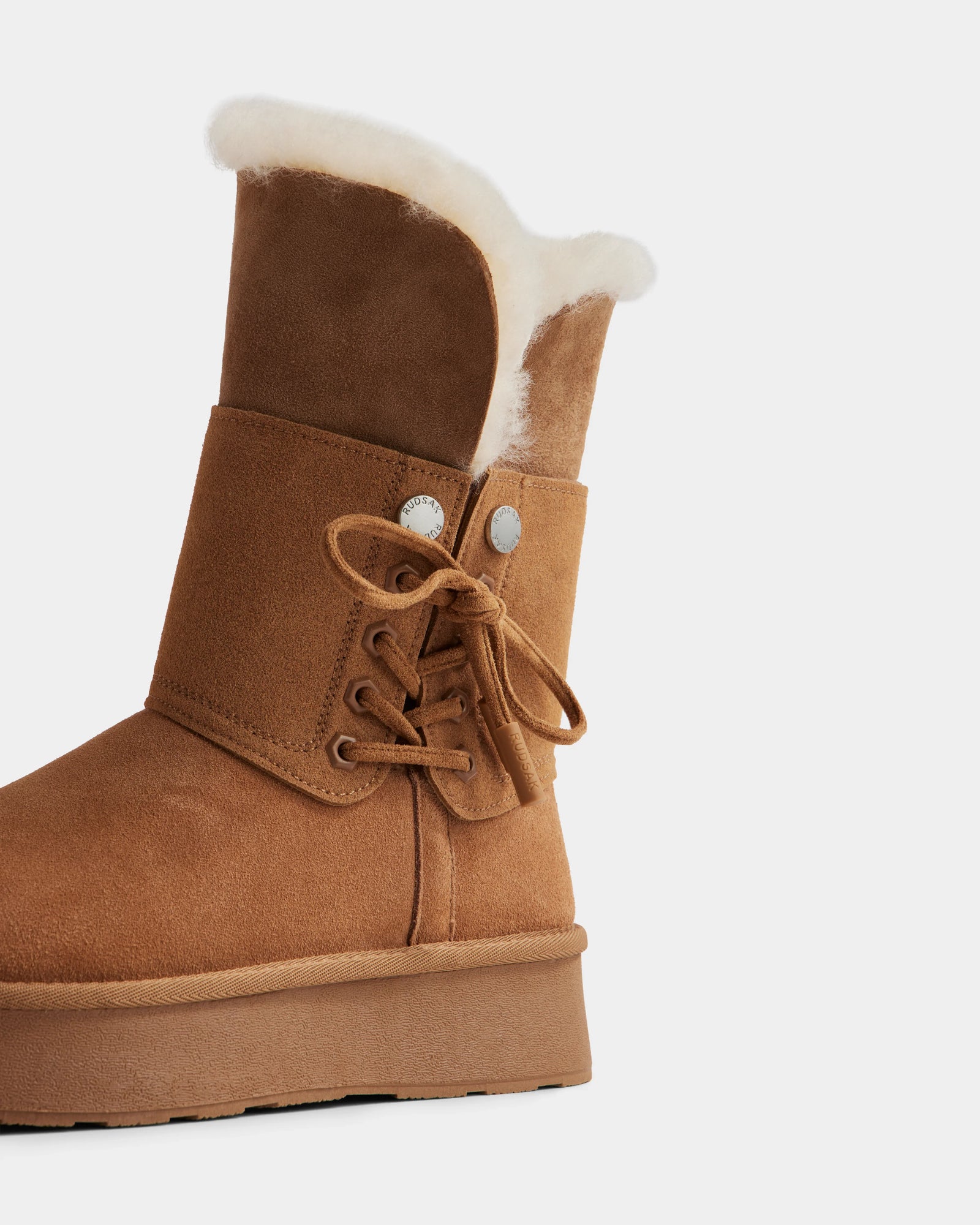 The Rudsak INESA - L225026 Tan is a women's brown suede platform boot with white faux fur lining, thick sole, side laces, and silver eyelets—stylish and cozy for winter. Shown on a plain white background.