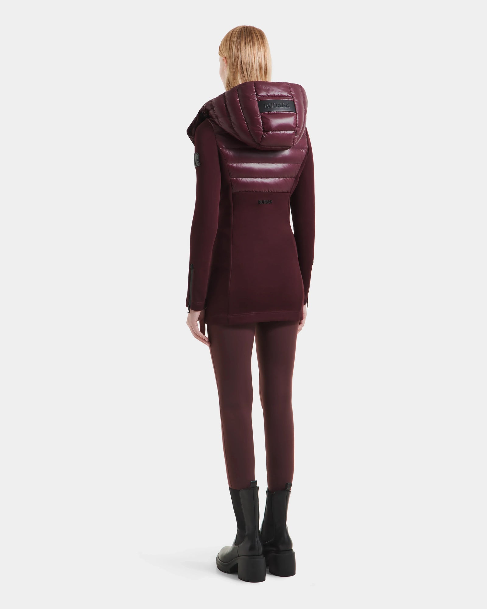 A person in the Rudsak MARRY S - L125521 Wine weather-resistant hooded coat stands facing away, paired with matching maroon leggings and black chunky boots, against a plain white background.
