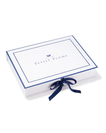 A rectangular white gift box with a blue border elegantly displays the Petite Plume brand, tied with a blue ribbon. The luxury of their Mens Silk Pajama Set in Black Art Nouveau offers the nightly charm of being wrapped in mulberry silk.