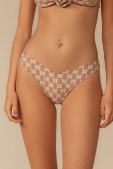 Beige lace bikini bottom with zig-zag stitching and geometric pattern, shown on model from waist to thigh.