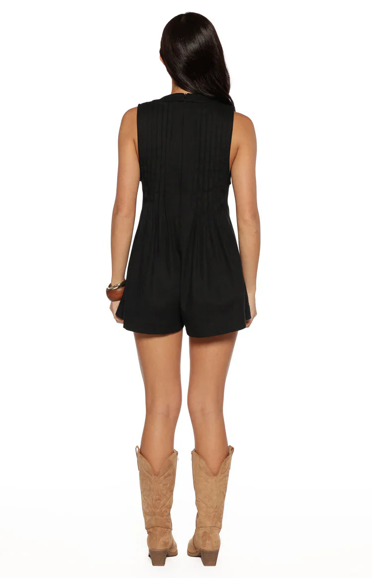Rear view of a black sleeveless playsuit with vertical pleats on the bodice and flowy shorts