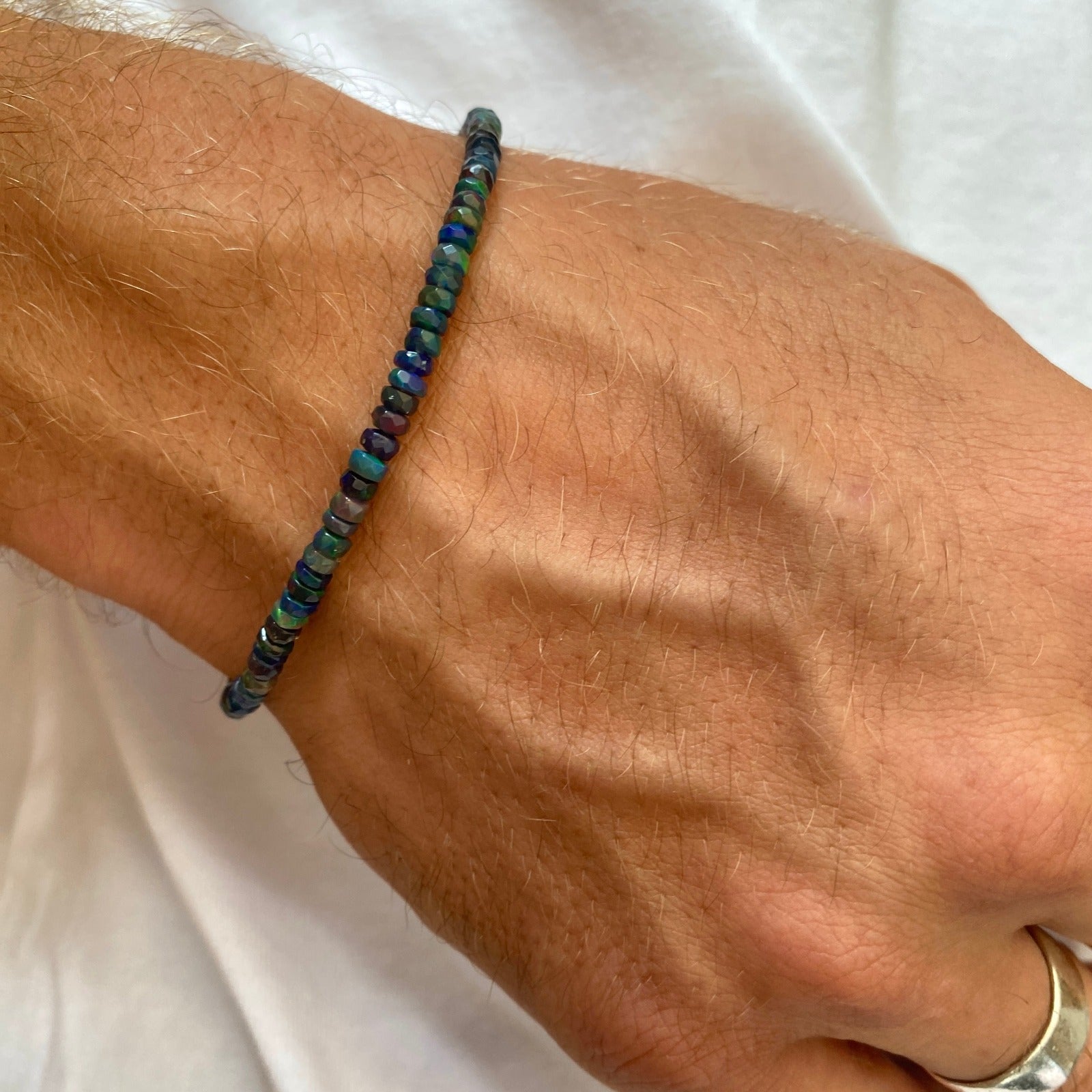 Shimmering beaded bracelet made of faceted opals in shades of black, blue, and green on a gold linking lobster clasp.