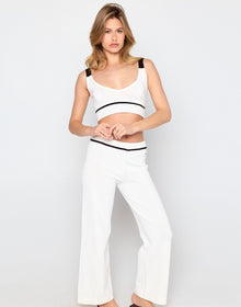 Woman wearing a white sleeveless top with black accents and white pants on a light gray background