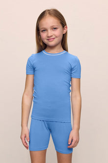 Model is wearing the Kids TENCEL Modal Unisex Short PJ Set in cornflower blue/white