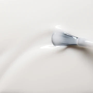 A close-up of a brush spreading smooth, white cream or lotion, creating gentle ripples on the creamy surface.