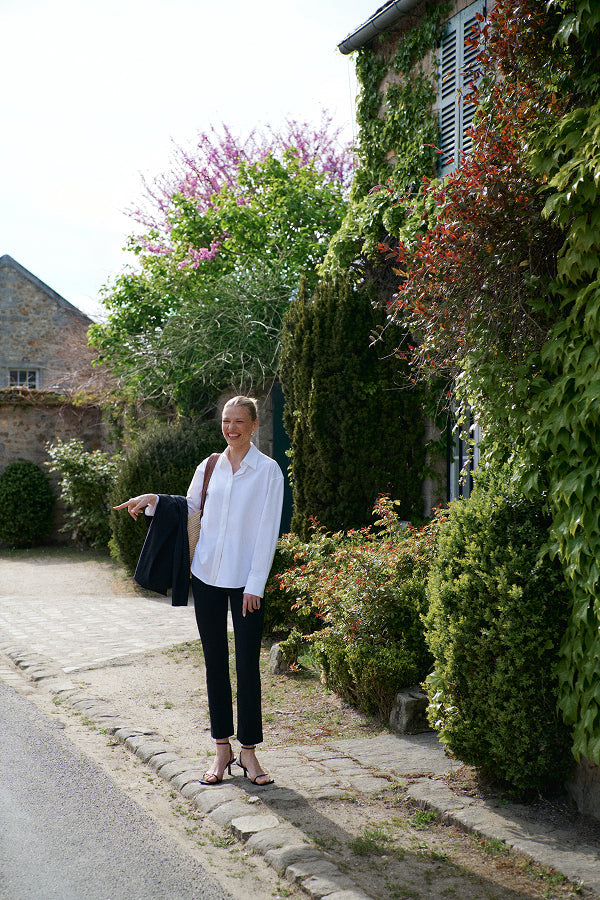 Woman standing on a street with greenery and a building in the background | Exclude