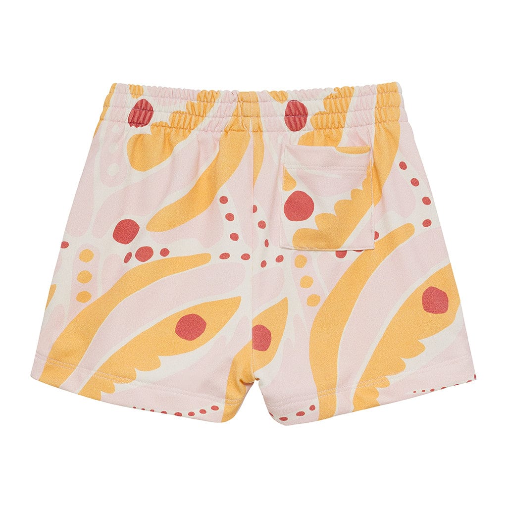 Pale pink swim trunk with yellow palm leaf and red circular motifs, elastic waistband, back pocket visible.