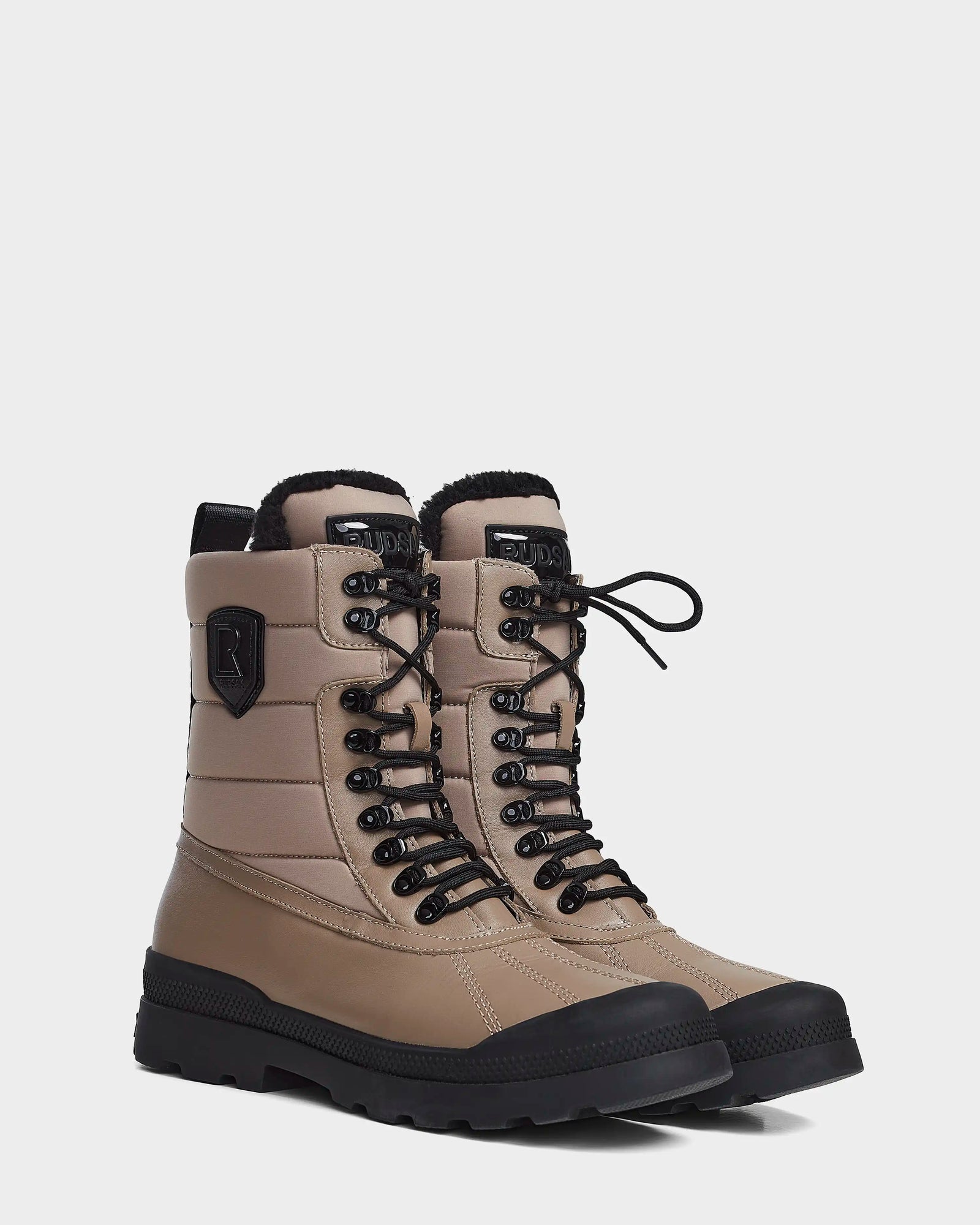 A pair of Rudsak REAGAN - 6222500 Cement men’s winter boots with padded uppers, black soles and eyelets, waterproof construction, and a black patch logo on the side, displayed on a plain white background.