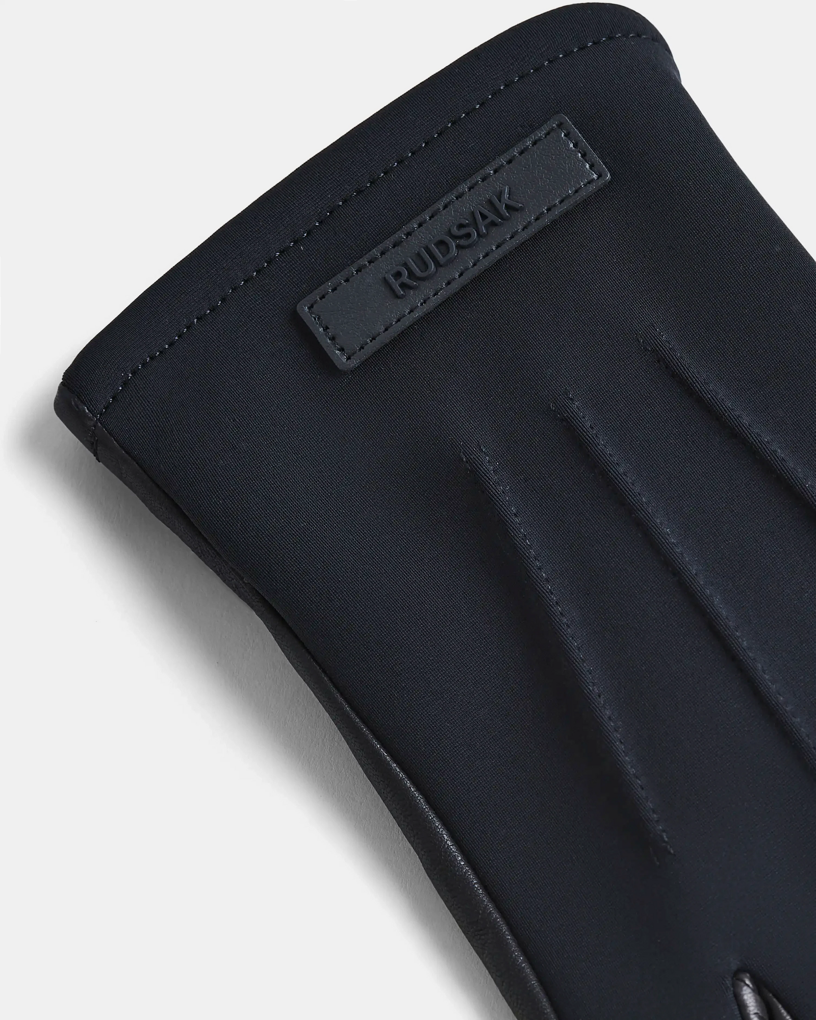 A close-up of the KRISTOPHER - 6423502 Black mens leather glove by Rudsak, showcasing detailed stitching and a rectangular patch embossed with the brand name, makes this accessory a standout in winter fashion against a light background.