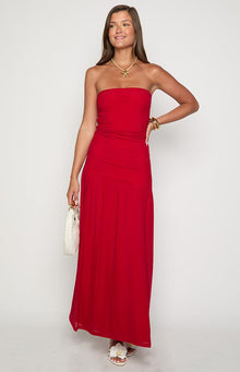  and earrings and carrying a small black handbag while standing against a textured white wall.