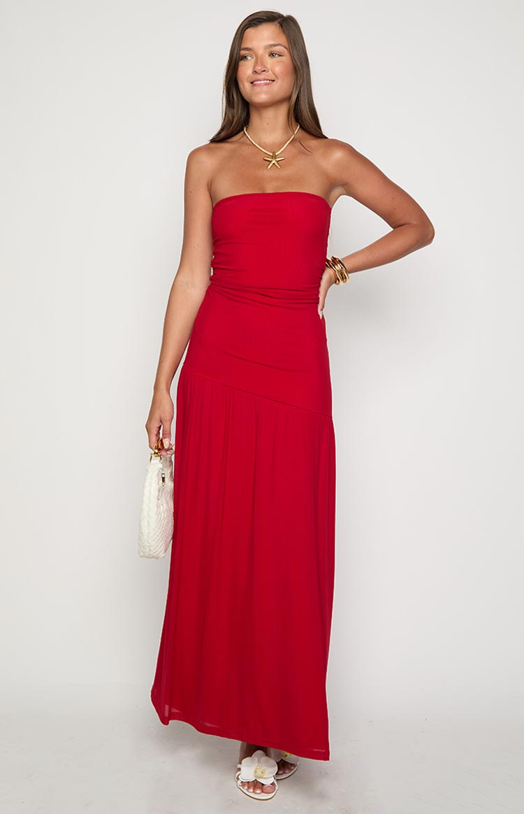  and earrings and carrying a small black handbag while standing against a textured white wall.