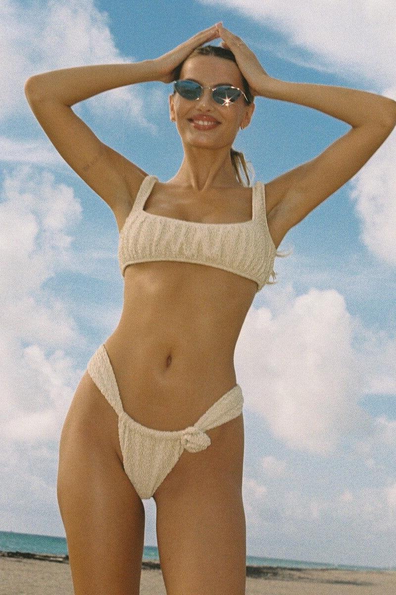 Cream textured bikini top with square neckline and thin straps on model at beach.