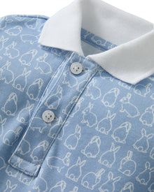 The Baby's Pima Louis Play Romper in Hoppy Days Blue is a light blue short-sleeve romper with a white collar and sleeve cuffs, a white bunny outline pattern, and bottom snaps for easy changing.