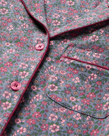The Women's Pima Pajama Set in Fleurs de Saison features long sleeves and a small floral print in pink, white, and blue on gray. The set includes a button-up top with a chest pocket and matching pants.
