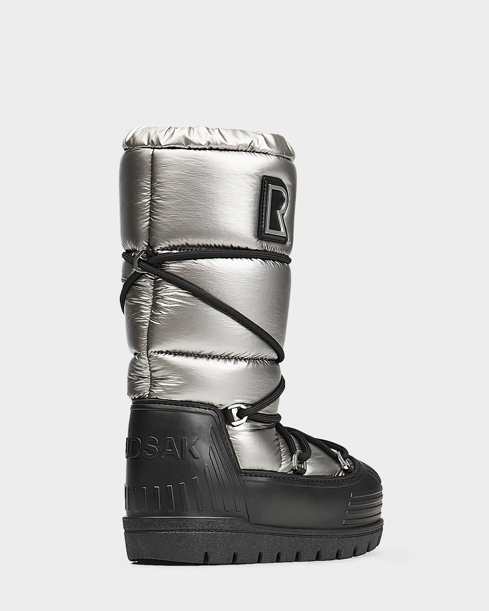 The Rudsak TISH - L223508 Pewter womens winter boot features a metallic silver and black design, thick platform sole, quilted upper, crisscross laces, and a logo patch on the side, shown against a plain light gray background.