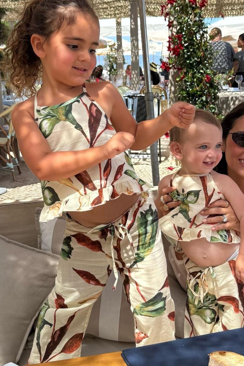 Child wearing cream-colored wide-leg pants with red and green floral print and matching halter top with drawstring waist.