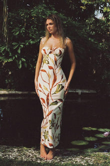 Long slip dress with red, gold, and green floral petal print on cream background, thin straps, fitted silhouette.