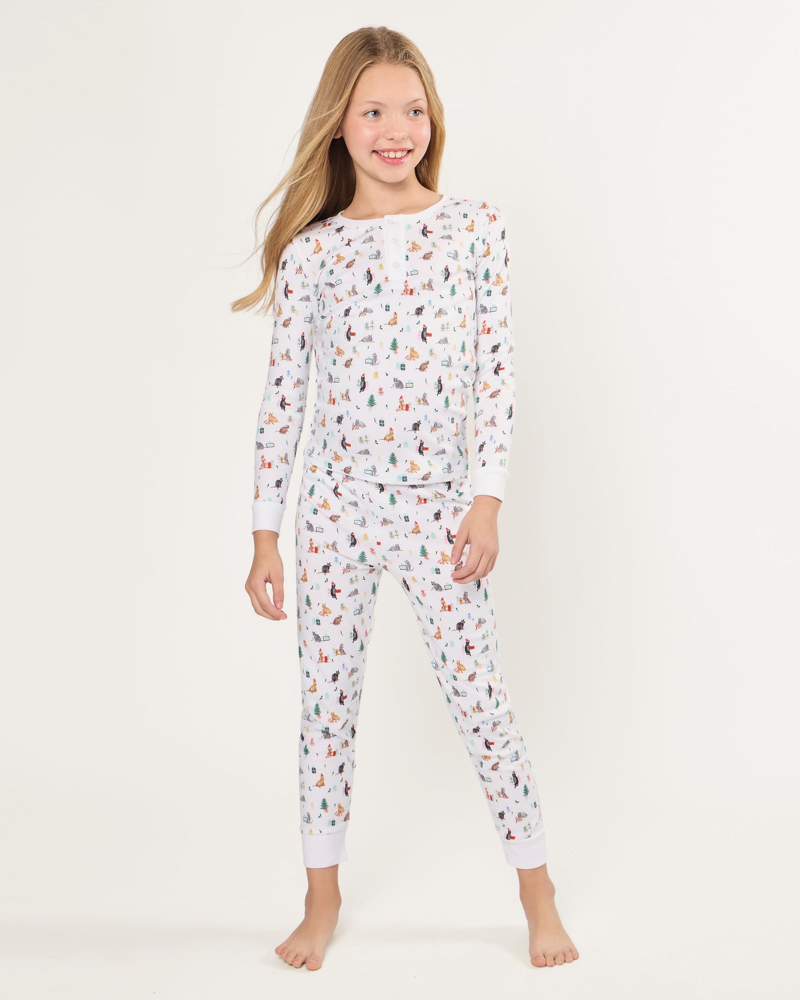 Kid's Pima Snug Fit Pajama Set in Merry Meow features a long-sleeve button-up top and matching pants with winter and holiday-themed prints of cats, trees, presents, and snowmen on a white background.
