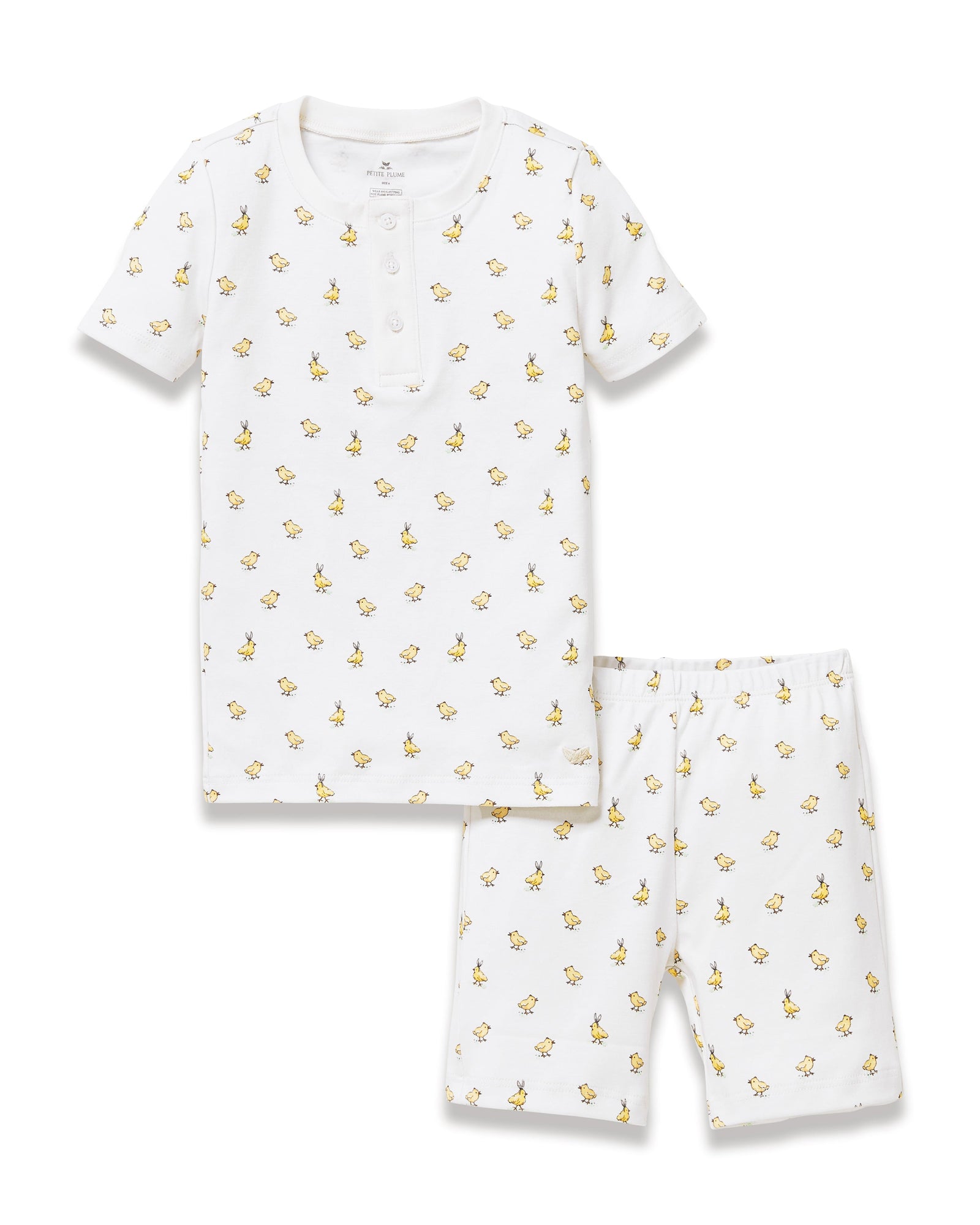 A young child with long brown hair smiles while wearing the Kid's Pima Snug Fit Short Set in Tres Chick, standing against a plain light background.