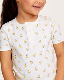 A young child with long brown hair smiles while wearing the Kid's Pima Snug Fit Short Set in Tres Chick, standing against a plain light background.