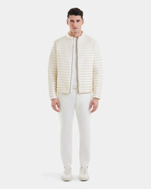 A man faces forward wearing Rudsaks REYMOND - M125013 Iceland mens down jacket, made from RDS-certified down and recycled nylon, paired with white pants and sneakers, set against a plain white background.